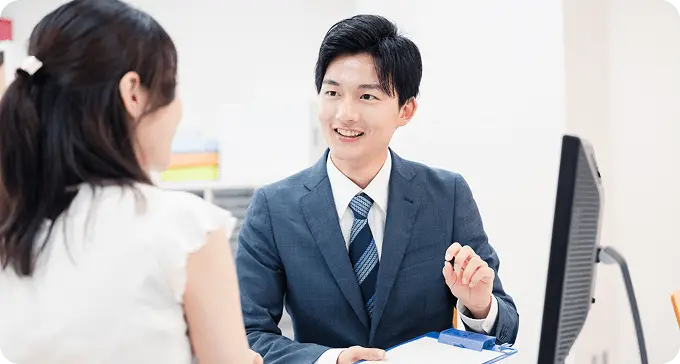 スーツ姿の男性がオフィスで女性に笑顔で説明している様子。丁寧な接客相談のイメージ。