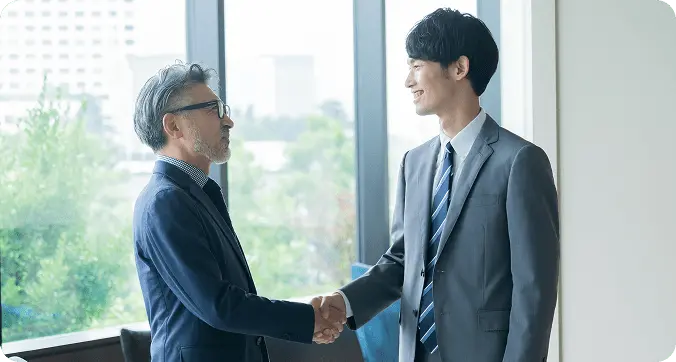 ビジネスシーンでスーツを着た2人の男性が握手を交わしている。契約成立や信頼関係の構築を表現。